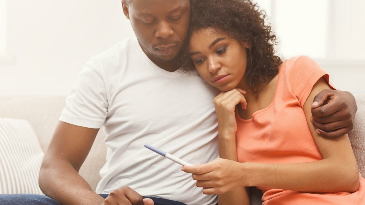 une femme dans les bras d'un homme, tenant un test de grossesse