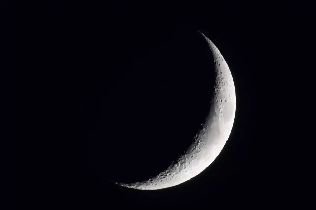 New moon in a clear night sky, showcasing a dark silhouette against the stars.