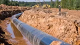 Conduite de pipeline en cours d’installation dans une tranchée, avec engins de chantier et ouvriers au loin