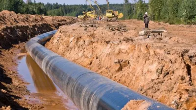 Conduite de pipeline en cours d’installation dans une tranchée, avec engins de chantier et ouvriers au loin