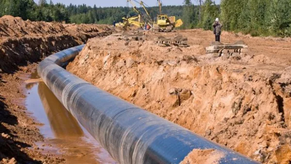 Conduite de pipeline en cours d’installation dans une tranchée, avec engins de chantier et ouvriers au loin