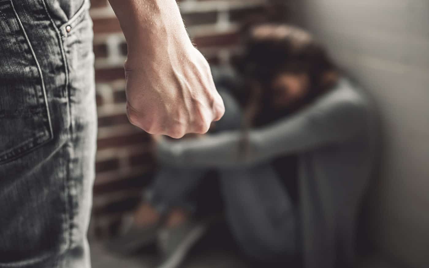 Femme frappée. Jeune fille assise sur le sol tandis que l'homme au premier plan serre le poing.