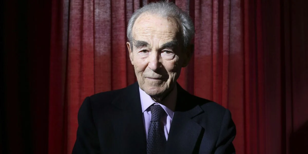 Robert Badinter, ancien ministre de la Justice, lors d'une conférence, souriant et pensif.