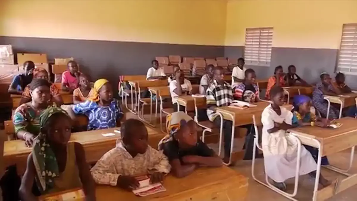Élèves en classe de cours primaire au Sénégal, enseignant en arrière-plan.