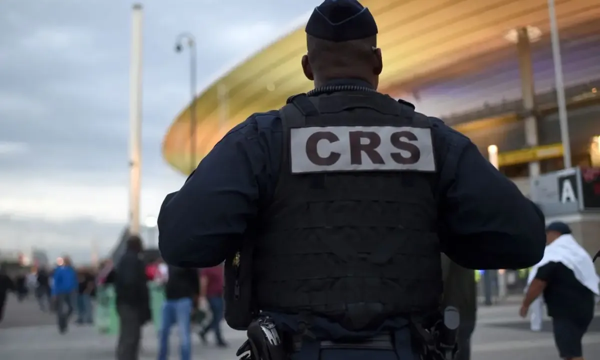 Agent de sécurité CRS de dos devant un stade, avec des passants en arrière-plan
