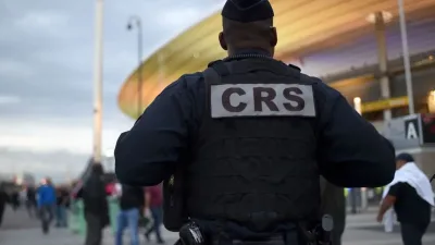 Agent de sécurité CRS de dos devant un stade, avec des passants en arrière-plan