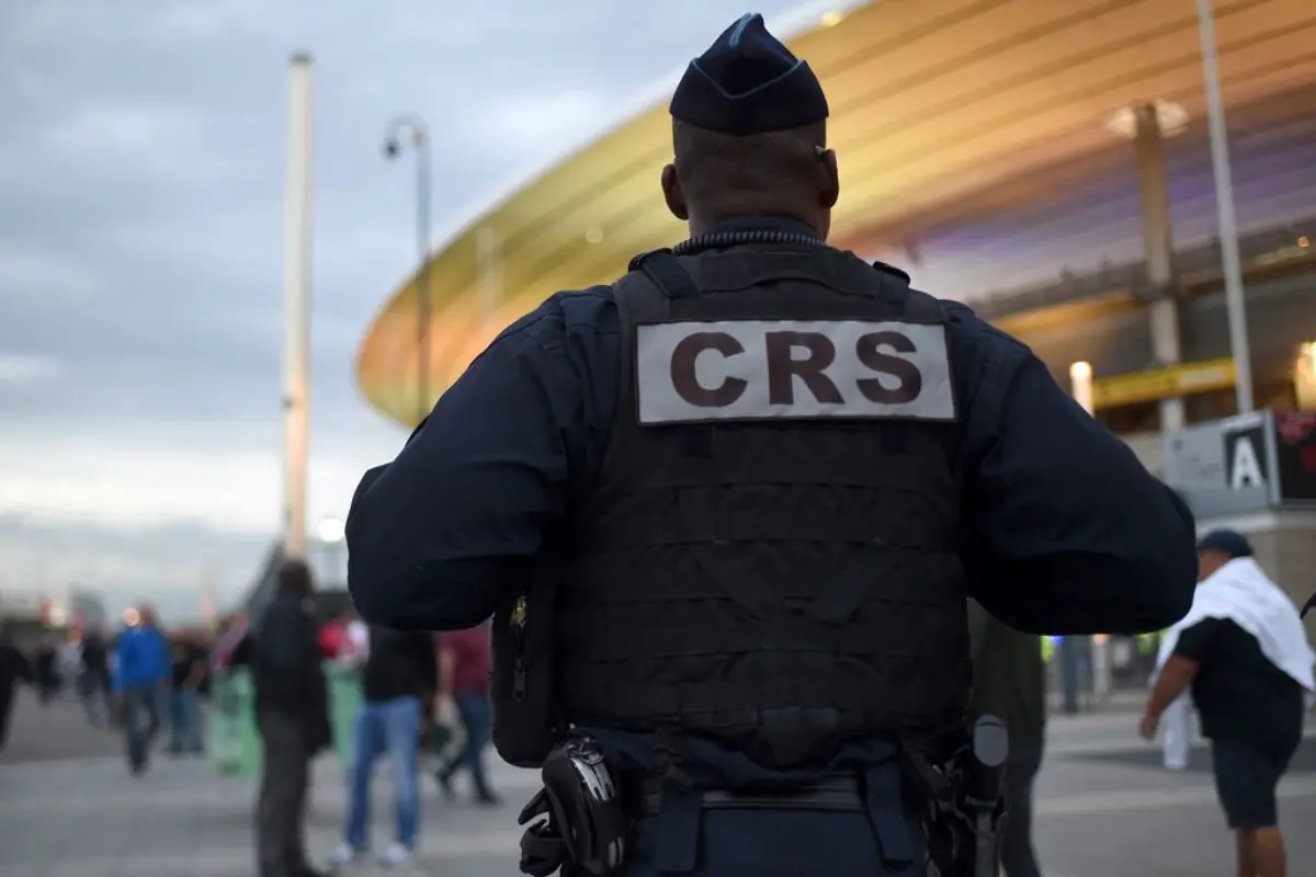 Agent de sécurité CRS de dos devant un stade, avec des passants en arrière-plan